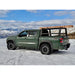 sideview of Green pickup truck with a bed rack carrying wood in a snowy landscape with mountains.