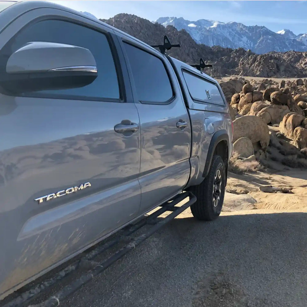Tacoma truck with rock sliders parked in a desert landscape with mountains in the background