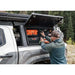 Person using a tool to open a storage compartment on a vehicle with a forest background
